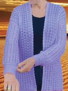 a woman standing in the desert wearing a purple crochet cardigan and holding a cell phone