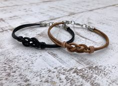 two brown and black leather bracelets sitting on top of a white wooden table next to each other