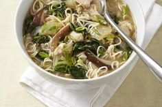 a white bowl filled with noodles and vegetables on top of a napkin next to a spoon