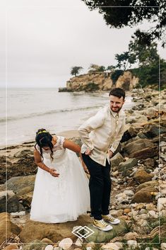 a bride and groom standing on rocks by the ocean with their feet in the air