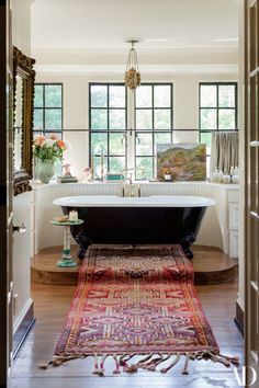 a bath tub sitting next to a wooden floor in a room with windows and rugs on the floor