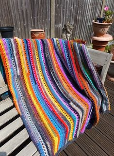 a multicolored crocheted blanket sitting on top of a wooden bench next to potted plants