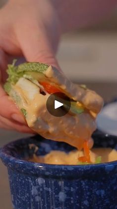 a person is dipping something into a blue bowl with food in it and holding the sandwich up to their face