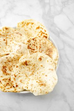 tortillas on a white plate sitting on a marble surface