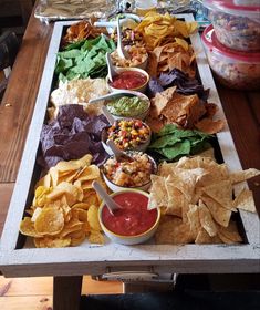 a tray filled with chips, salsa and guacamole on top of a wooden table