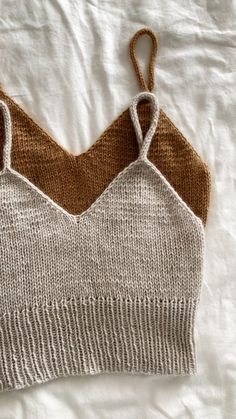 two knitted bras laying on top of a white bed with brown trimming