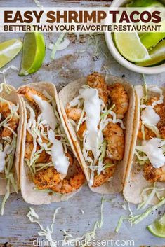 three shrimp tacos with lime wedges on the side