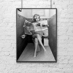 a black and white photo of a woman sitting on a toilet reading a newspaper in the bathroom