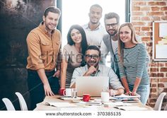 a group of people standing around a table in front of a laptop and coffee mugs