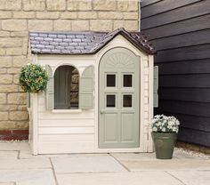 a small dog house sitting next to a brick building with flowers growing out of it