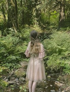 a woman in a pink dress is walking through the woods with her back to the camera