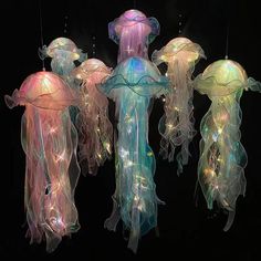 three jellyfish lights hanging from strings in the dark, one is multicolored