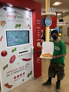 a man wearing a face mask holding a pizza box in front of a vending machine