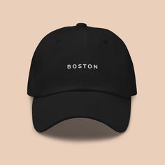 the boston hat is black with white lettering on it and sits against a beige background