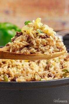 a wooden spoon filled with rice and meat on top of a pan next to peppers