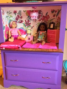 two dolls sitting on top of a purple dresser