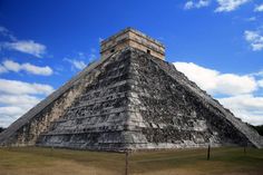 an ancient pyramid in the middle of a grassy area under a blue sky with clouds