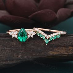 two rings with green and white stones are on a piece of wood next to a flower