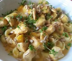 a white bowl filled with pasta covered in sauce and garnished with parsley