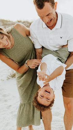 a man and woman holding a small child on their back while standing in the sand