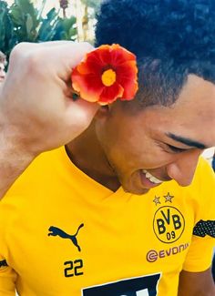 a man with a flower in his hair is smiling at the camera while wearing a yellow shirt