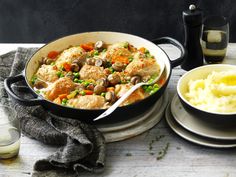 a pan filled with meat and vegetables next to a bowl of mashed potatoes on a table