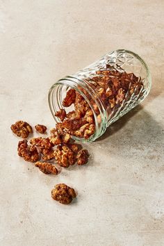 a glass jar filled with nuts sitting on top of a white counter next to a pile of walnuts