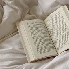 an open book sitting on top of a bed covered in white sheets and blankets,