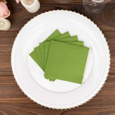 four green napkins sitting on top of a white plate next to candles and flowers