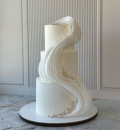 a three tiered white wedding cake with pearls on top