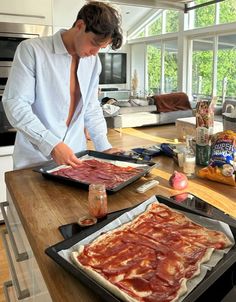 a man standing in front of two trays of food on top of a kitchen counter