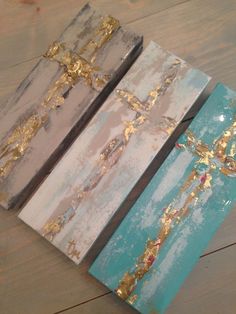 three paintings with gold paint on them sitting on top of a wooden table next to each other