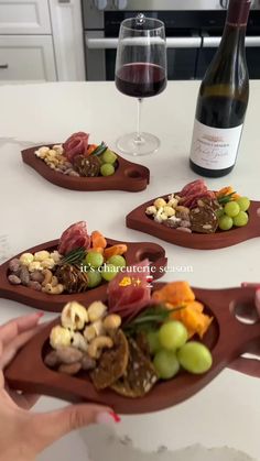 three wooden trays with different types of food on them and a bottle of wine in the background