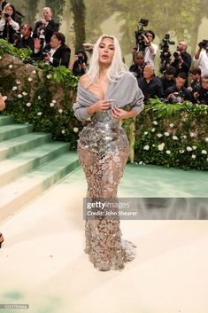 lady in silver dress standing on white carpet with cameras around her and people taking pictures