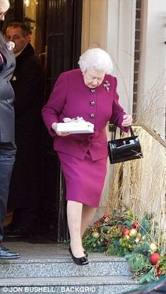 an older woman in a purple dress carrying a cake while walking out of a building