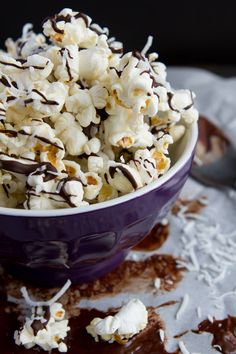 a purple bowl filled with white and chocolate popcorn on top of a doily covered table