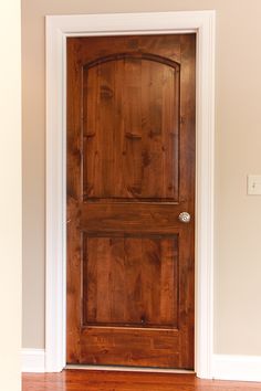 an empty room with a wooden door and hard wood flooring