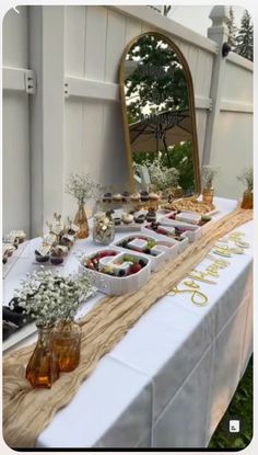 an outdoor buffet table is set up with flowers and fruit in vases on it