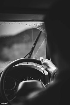 a person driving a car in the rain with their hand on the steering wheel and windshield