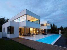 a large swimming pool in front of a modern house at dusk with the lights on