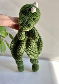 a crocheted green dinosaur stuffed animal sitting on top of a white table next to a plant