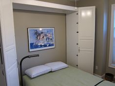 a bed sitting in a bedroom next to two windows and a painting on the wall