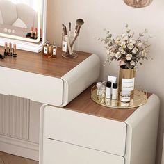 a white vanity with two drawers and a mirror on the wall next to it is a vase with flowers