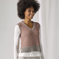 a woman standing in front of a white backdrop wearing a sweater and pants with an afro