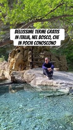 a man sitting on top of a rock next to a body of water with a sign above it