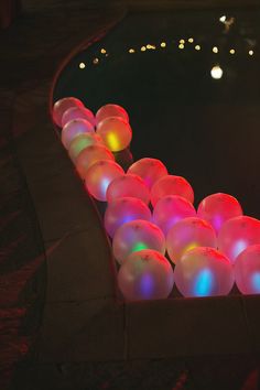 there are many glowing balls on the ground in front of a pool that is lit up with colored lights