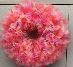 a pink and white frilly wreath hanging on a wall