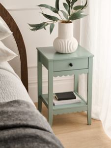 a small table with a plant on it next to a bed