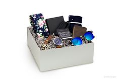 a white box filled with assorted items on top of a white table next to a pair of sunglasses