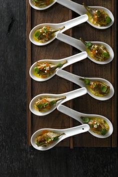 several spoons filled with food on top of a wooden tray next to utensils